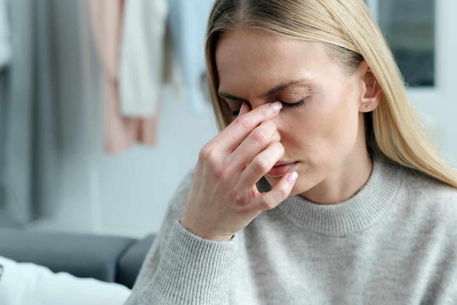 Frau reibt sich die geröteten, trockenen Augen am Bildschirmarbeitsplatz als Zeichen des Sicca-Syndroms